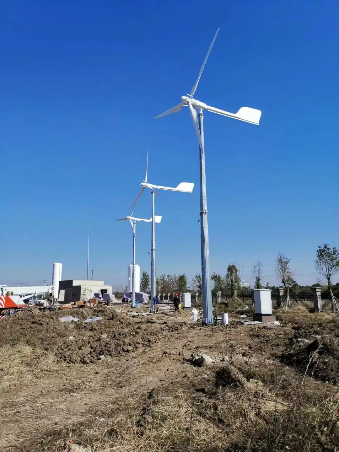 Complete horizontal-axis wind turbines with three-blade rotors, nacelles, tail vanes and full towers at a supplier installation site